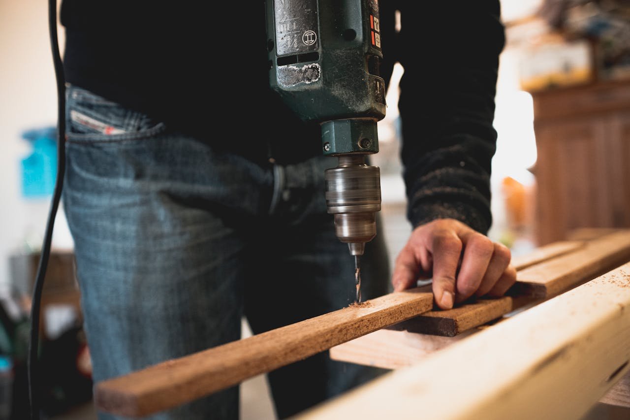 who-we-are Close-up of a person using an electric drill on a wooden plank, showcasing detailed woodworking skills.